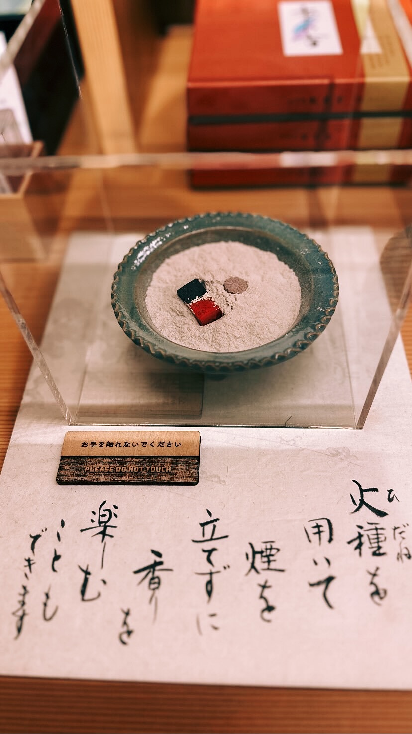 青みを帯びた皿に灰を敷き、火種を用いるためのしつらえが置かれた展示
